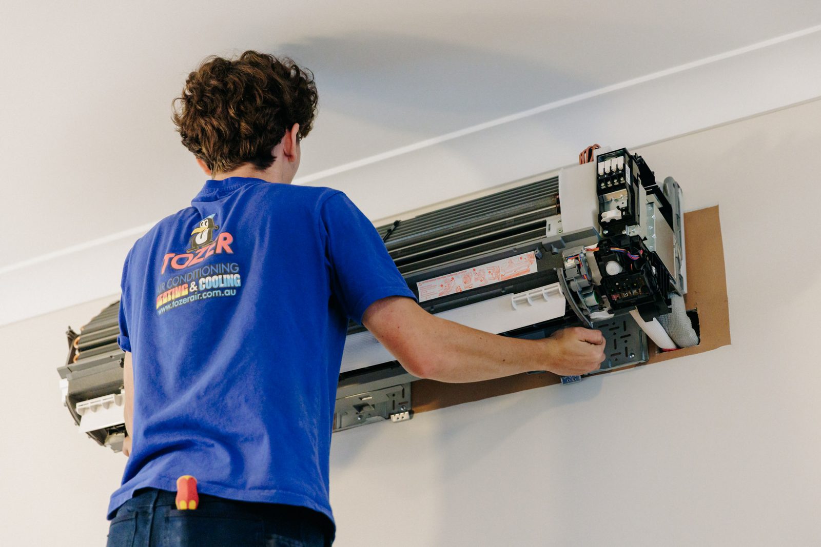 A Tozer Air technician fitting a wall-mounted split system inside a Newcastle home