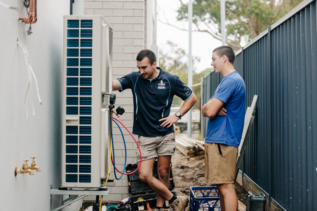 Two Tozer Air technicians installing outdoor units beside a Newcastle home
